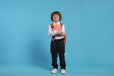 Happy schoolboy with backpack and books on light blue background