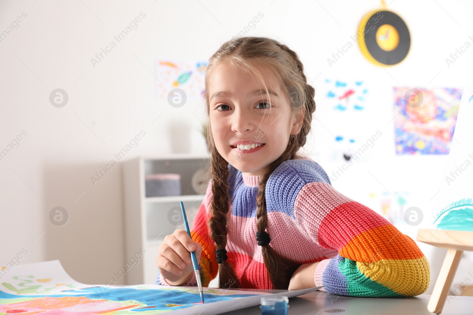 Photo of Little girl painting picture at table indoors