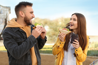 Happy young couple with sandwiches and coffee on city street