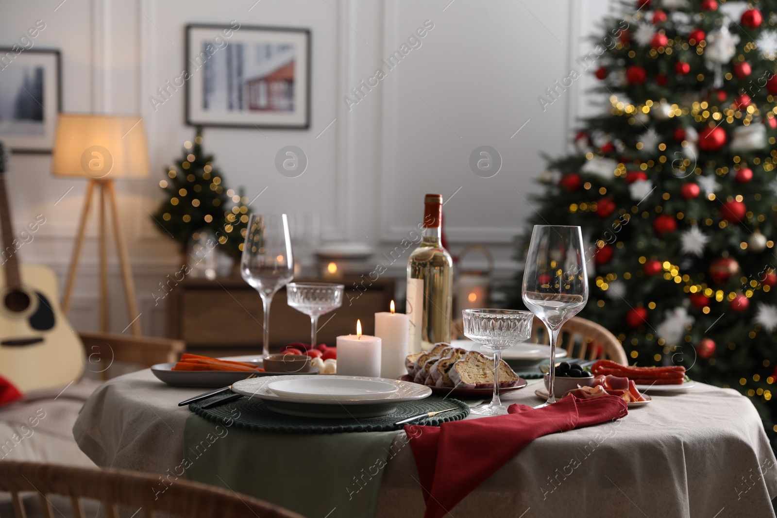 Photo of Christmas table setting with burning candles, appetizers and dishware in room