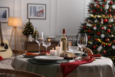 Photo of Christmas table setting with burning candles, appetizers and dishware in room