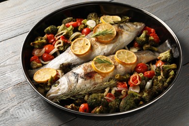 Photo of Baked fish with vegetables, rosemary and lemon on grey wooden table, closeup