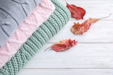 Photo of Stack of soft knitted sweaters on white wooden table, closeup