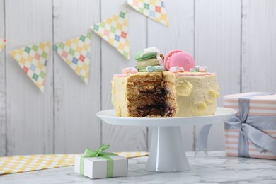 Delicious cake decorated with macarons and marshmallows and gift boxes on white marble table, space for text