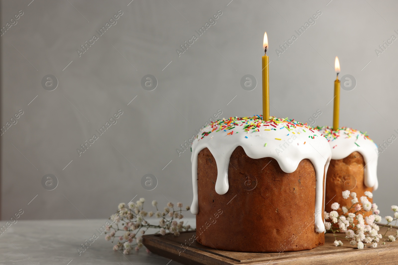 Photo of Tasty Easter cakes with burning candles on grey table. Space for text