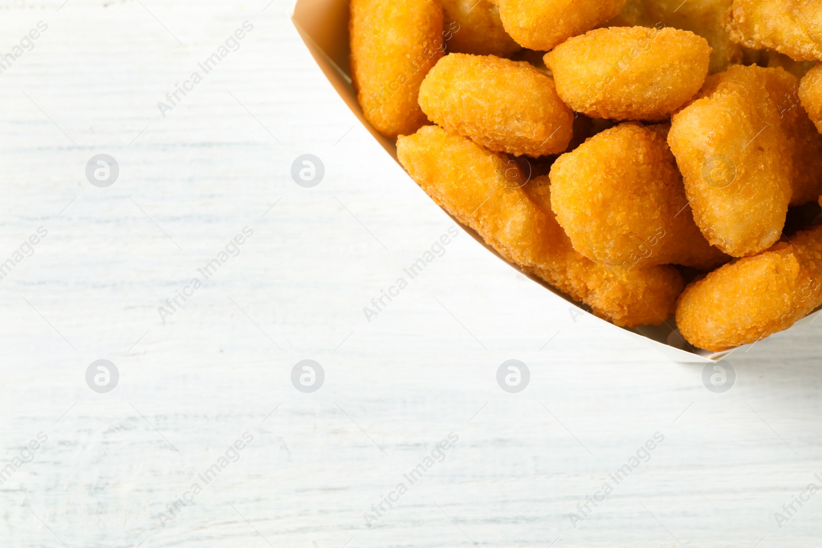 Photo of Tasty fried chicken nuggets on white wooden table, top view. Space for text
