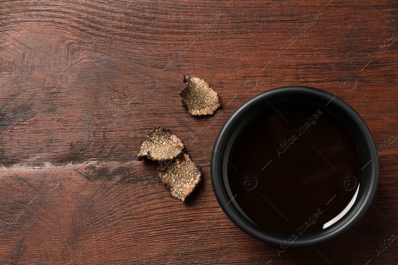 Photo of Fresh truffle oil in bowl on wooden table, flat lay. Space for text