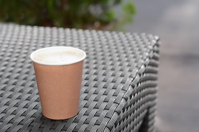 Photo of Cardboard cup with coffee on rattan table outdoors, space for text