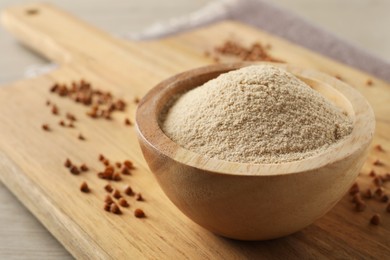 Photo of Bowl of buckwheat flour on white wooden table, closeup. Space for text