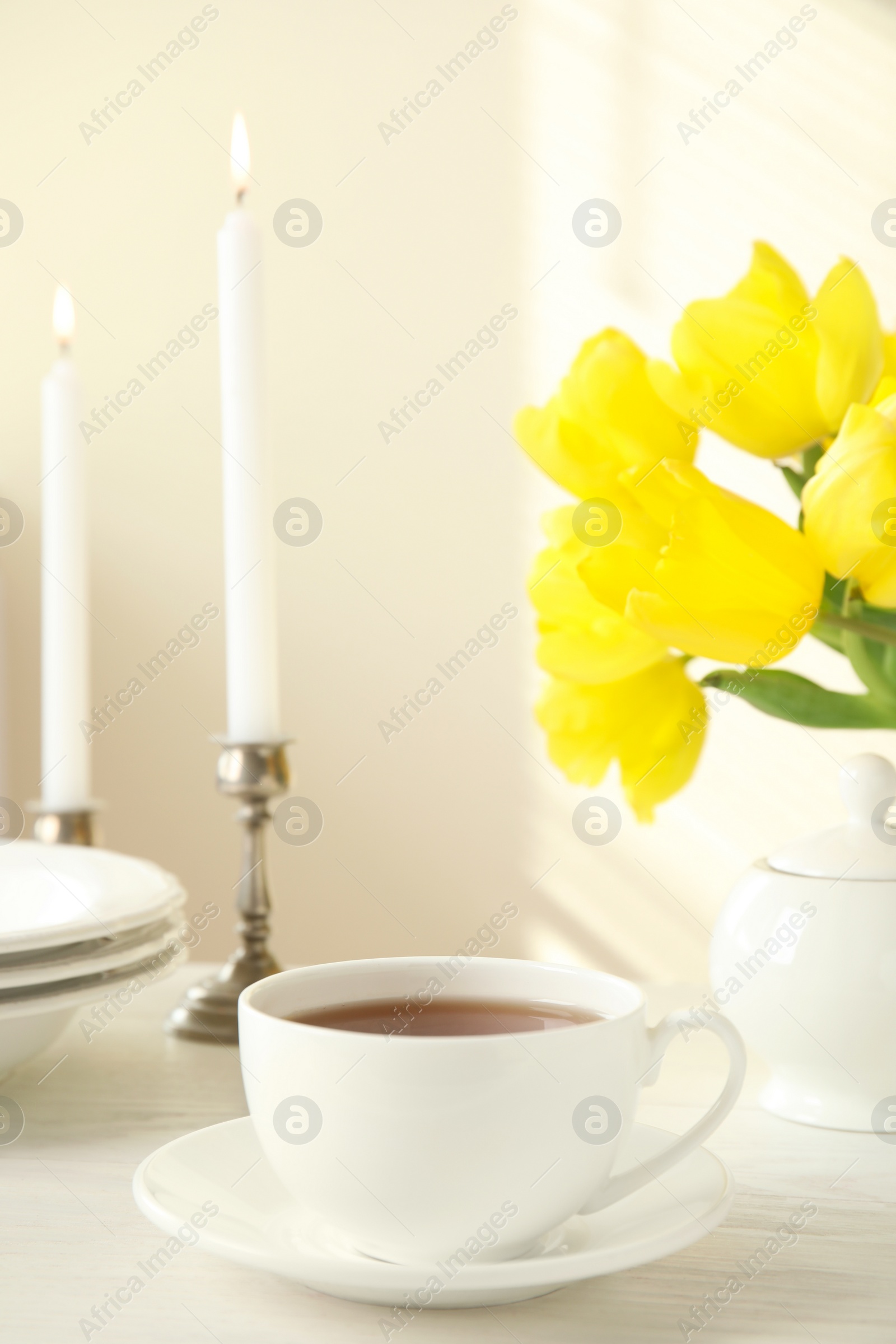 Photo of Tea set, candles and flowers on white wooden table