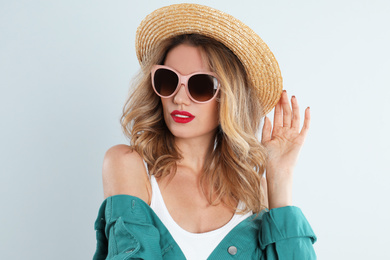 Young woman wearing stylish sunglasses and hat on light grey background