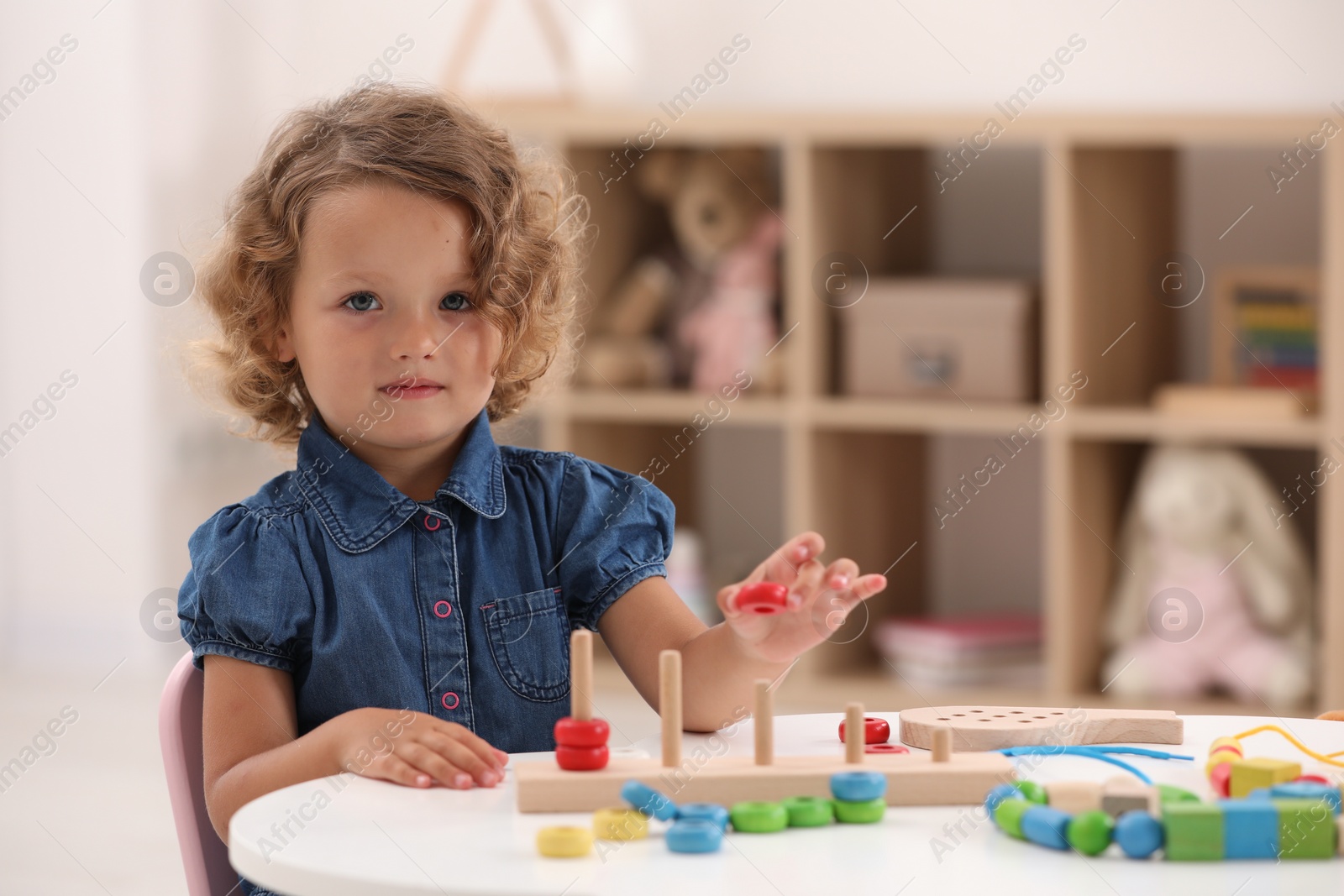 Photo of Motor skills development. Little girl playing with stacking and counting game at table indoors