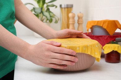 Photo of Woman holding bowl covered with beeswax food wrap at white table, closeup