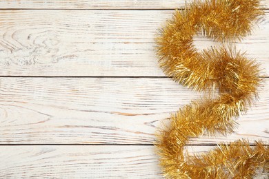 Photo of Golden tinsel on white wooden background, top view. Space for text