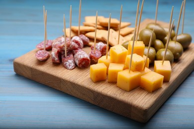 Photo of Toothpick appetizers. Pieces of cheese, sausage, olives and crackers on light blue wooden table, closeup