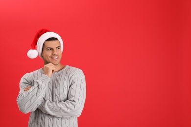 Handsome man wearing Santa hat on red background, space for text