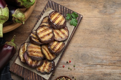 Photo of Delicious grilled eggplant slices on wooden table, flat lay. Space for text