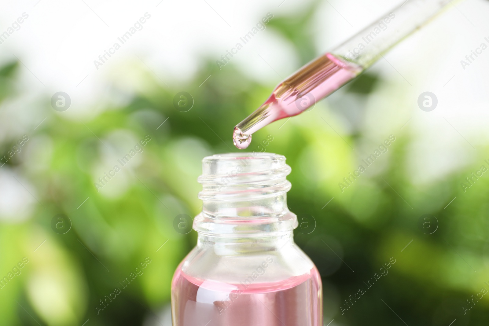 Photo of Dropper with essential oil over bottle against blurred background, closeup