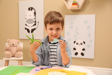 Photo of Little boy with scissors and cut paper cloud at table indoors