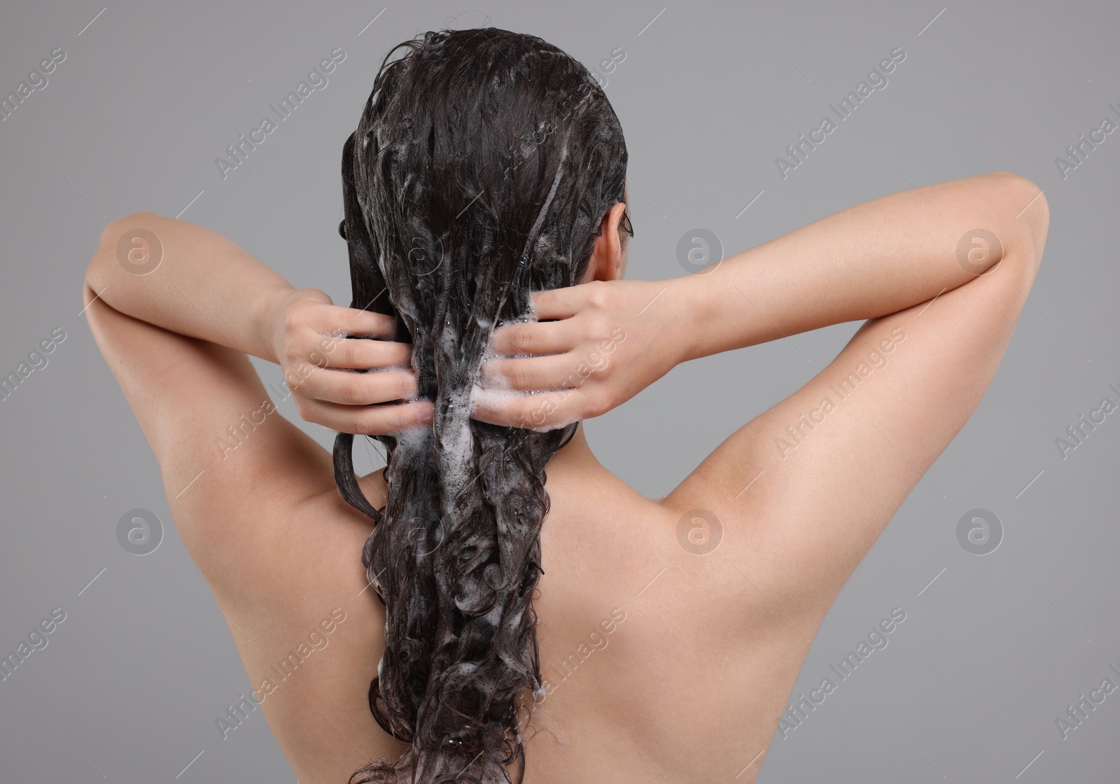 Photo of Woman washing hair on grey background, back view