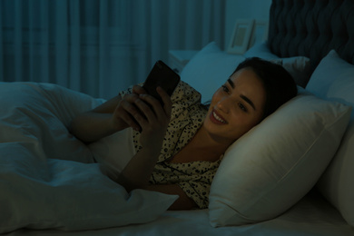 Photo of Young woman addicted to smartphone in bed at night