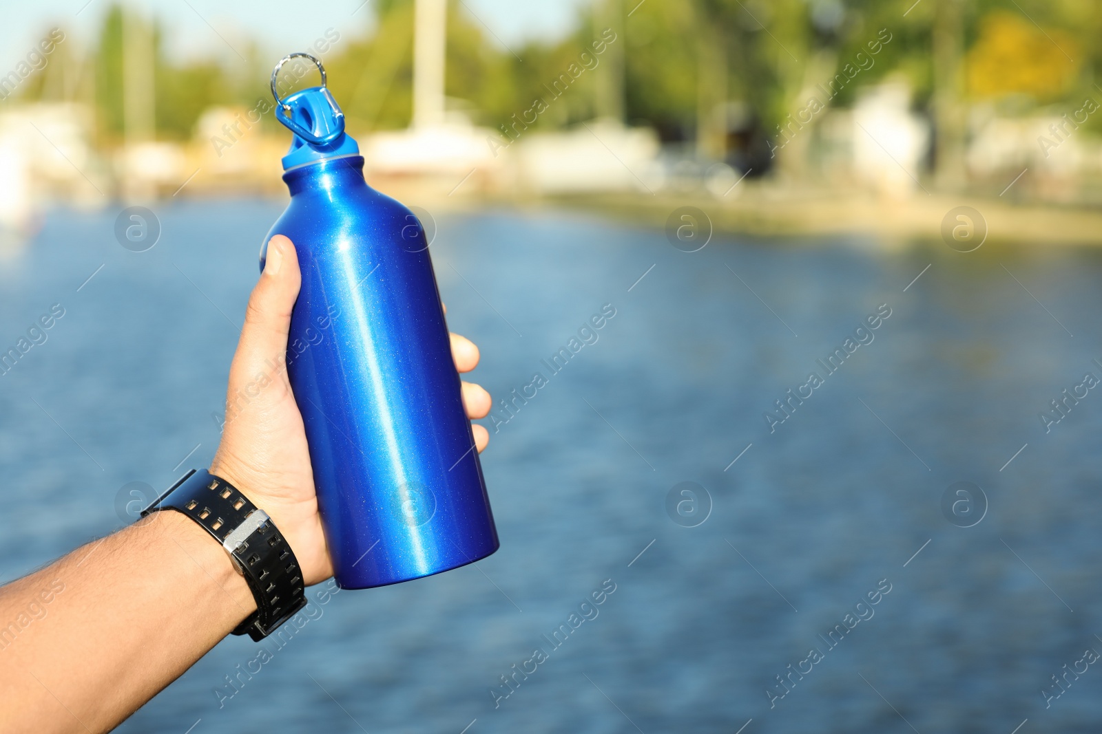 Photo of Young sporty man holding water bottle near river on sunny day. Space for text