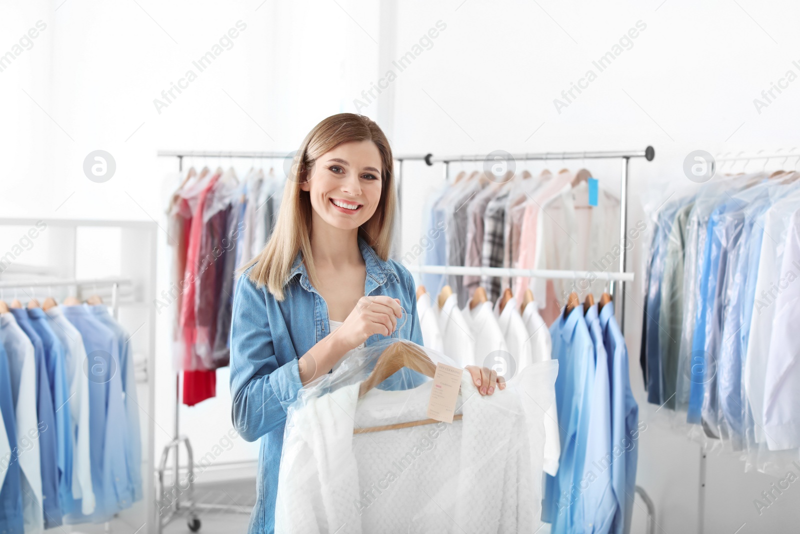 Photo of Young woman holding hanger with clothes in plastic bag at dry-cleaner's