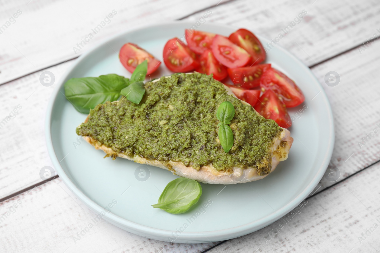 Photo of Delicious chicken breast with pesto sauce, tomatoes and basil on white wooden table, closeup