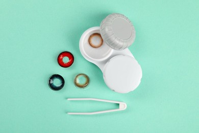 Different color contact lenses, tweezers and case on turquoise background, flat lay