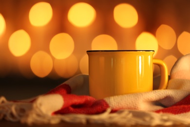 Cup of hot drink on scarf against blurred background. Winter atmosphere