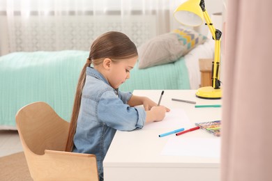 Photo of Cute little girl drawing with markers at desk in room. Home workplace