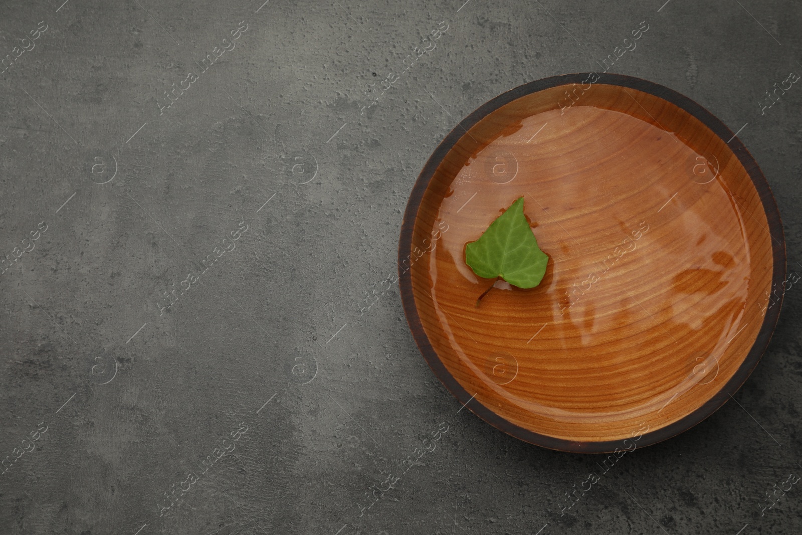 Photo of Wooden bowl with water and green leaf on grey table, top view. Space for text