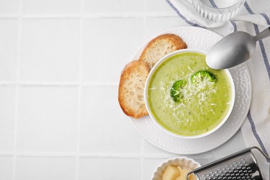 Photo of Delicious broccoli cream soup with cheese served on white tiled table, flat lay. Space for text