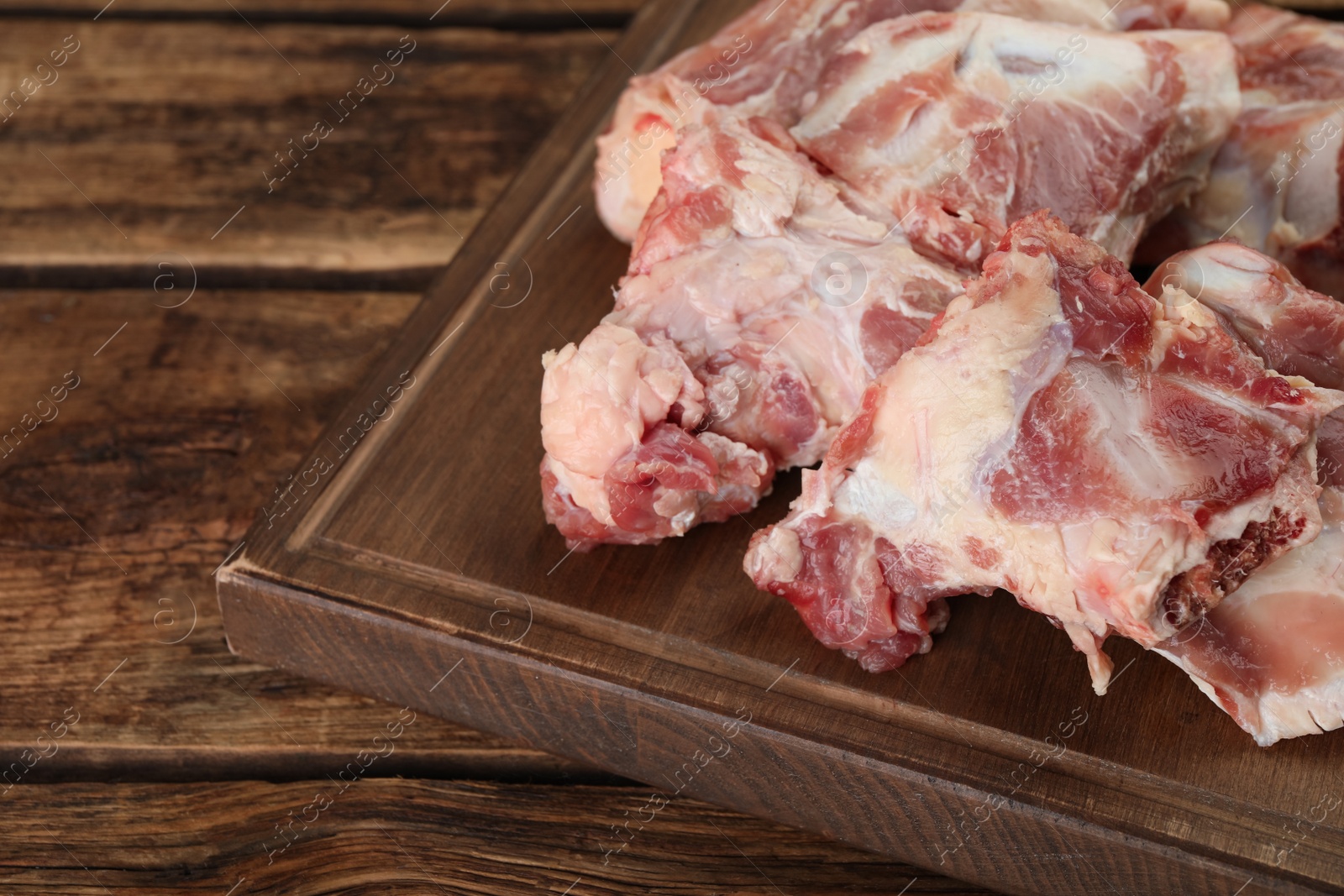 Photo of Cutting board with raw chopped meaty bones on wooden table. Space for text