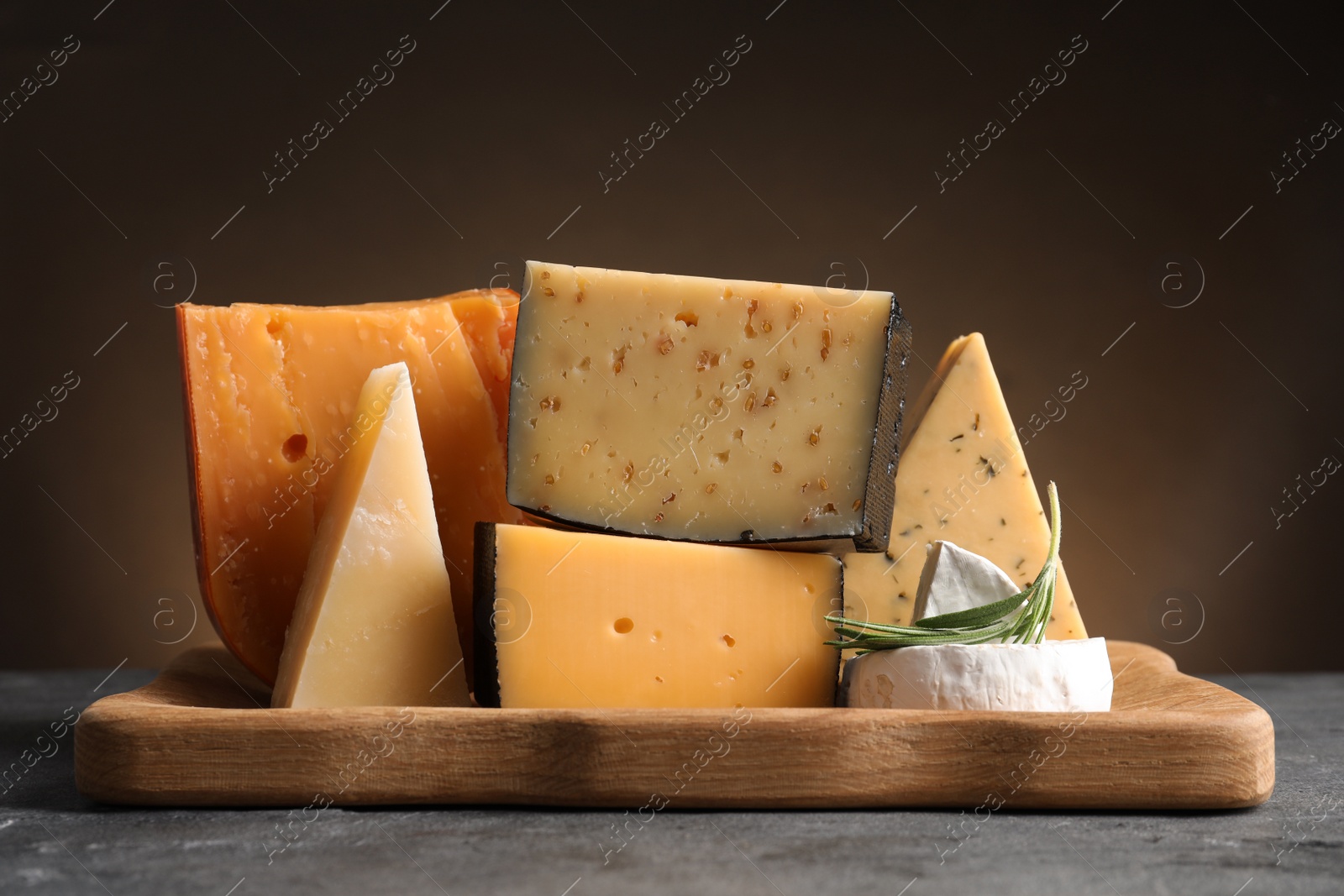 Photo of Wooden tray with different sorts of cheese and rosemary on grey table