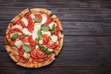 Photo of Delicious Caprese pizza with tomatoes, mozzarella and basil on dark wooden table, top view. Space for text