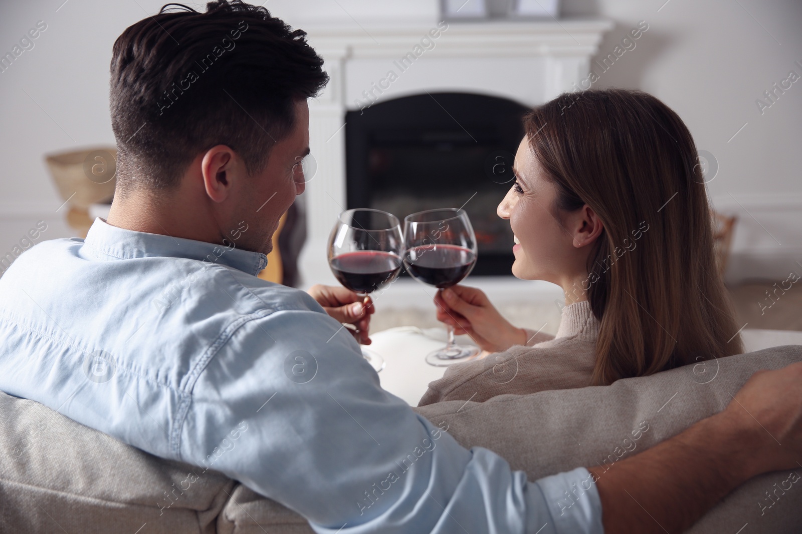 Photo of Happy couple with glasses of wine resting on sofa near fireplace at home