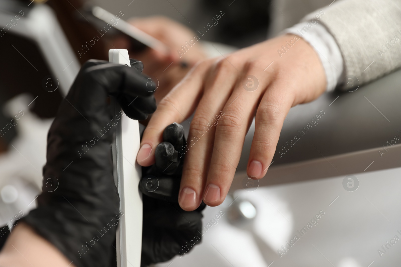 Photo of Professional manicurist filing client's nails in beauty salon, closeup