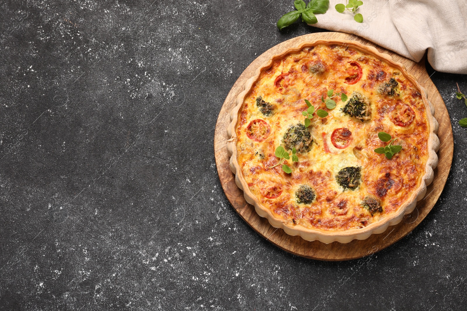 Photo of Delicious homemade vegetable quiche and oregano on black table, top view. Space for text