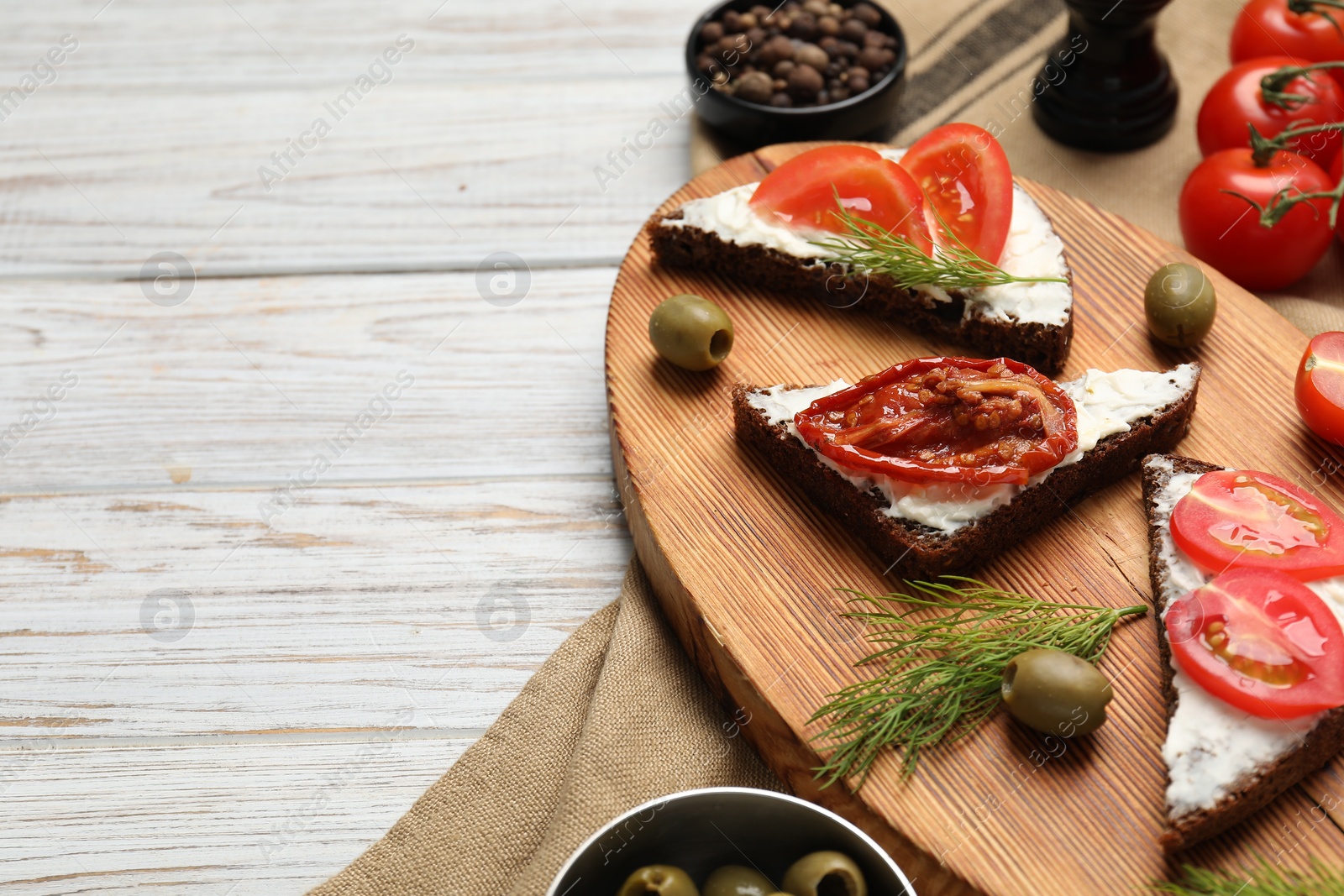 Photo of Delicious bruschettas with ricotta cheese, dill, olives, fresh and sun dried tomatoes on light wooden table, above view. Space for text