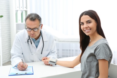 Doctor checking young woman's pulse with medical device in hospital