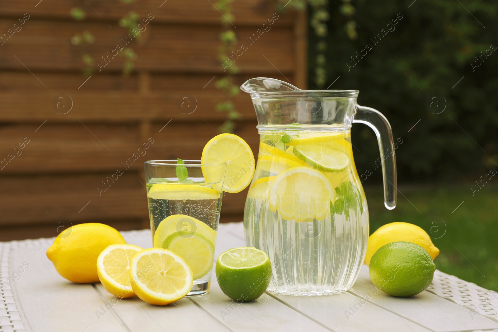 Photo of Water with lemons and limes on white wooden table outdoors