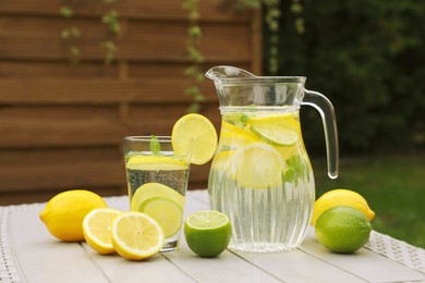 Photo of Water with lemons and limes on white wooden table outdoors