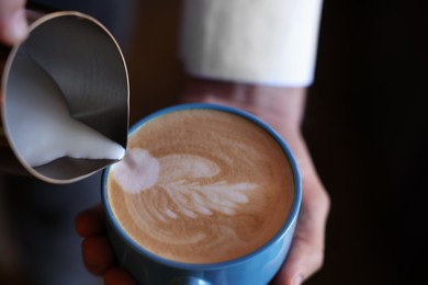 Photo of Barista pouring milk into cup of coffee on black background, closeup. Space for text