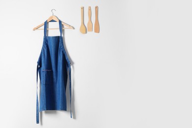 Denim apron and kitchen tools on light wall. Space for text