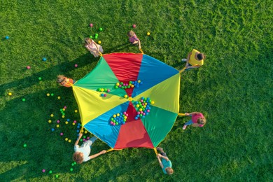 Photo of Group of children and teachers playing with rainbow playground parachute on green grass, top view. Summer camp activity
