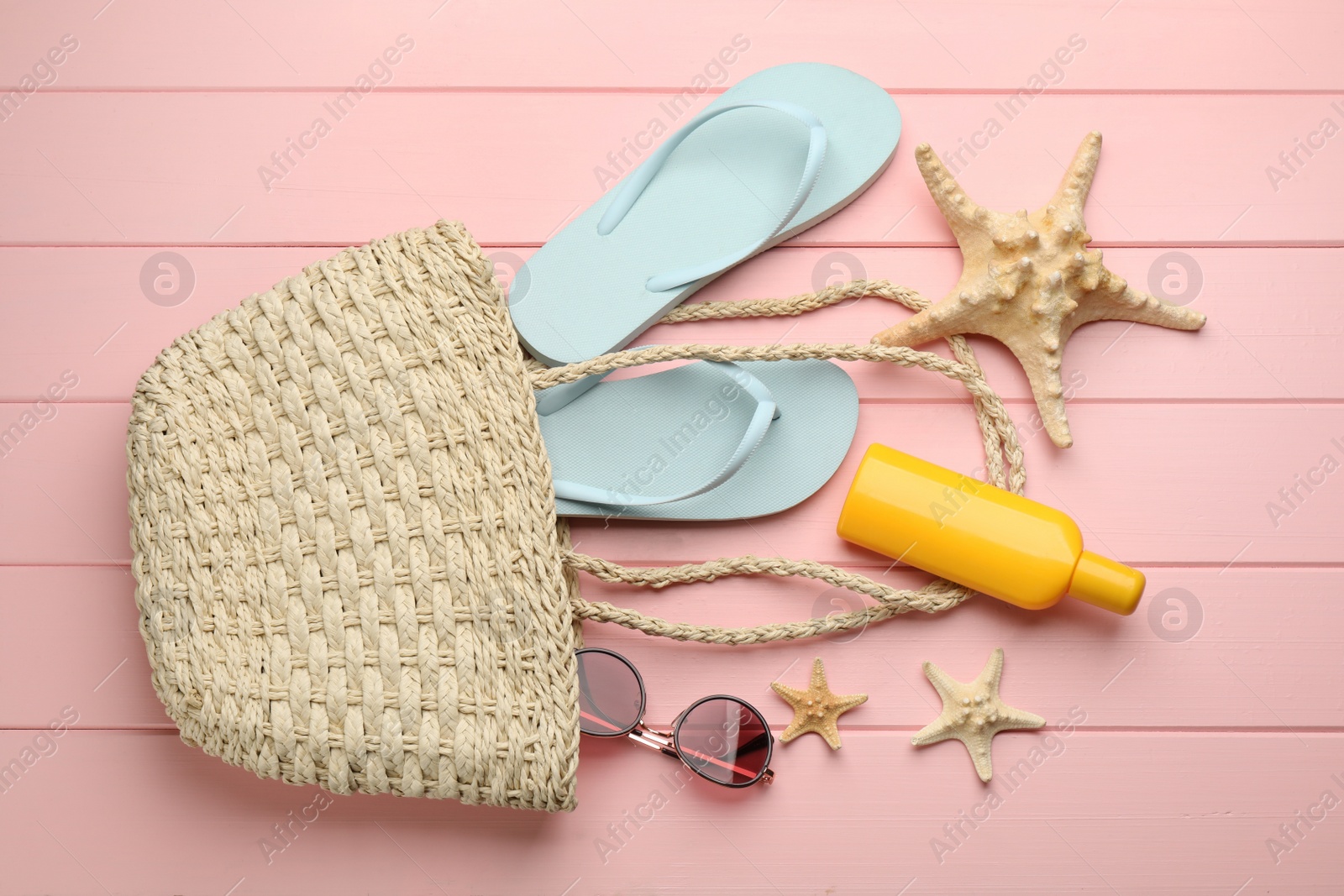 Photo of Stylish bag and beach accessories on pink wooden background, flat lay