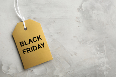 Photo of Top view of blank golden tag on light grey stone background, space for text. Black Friday concept