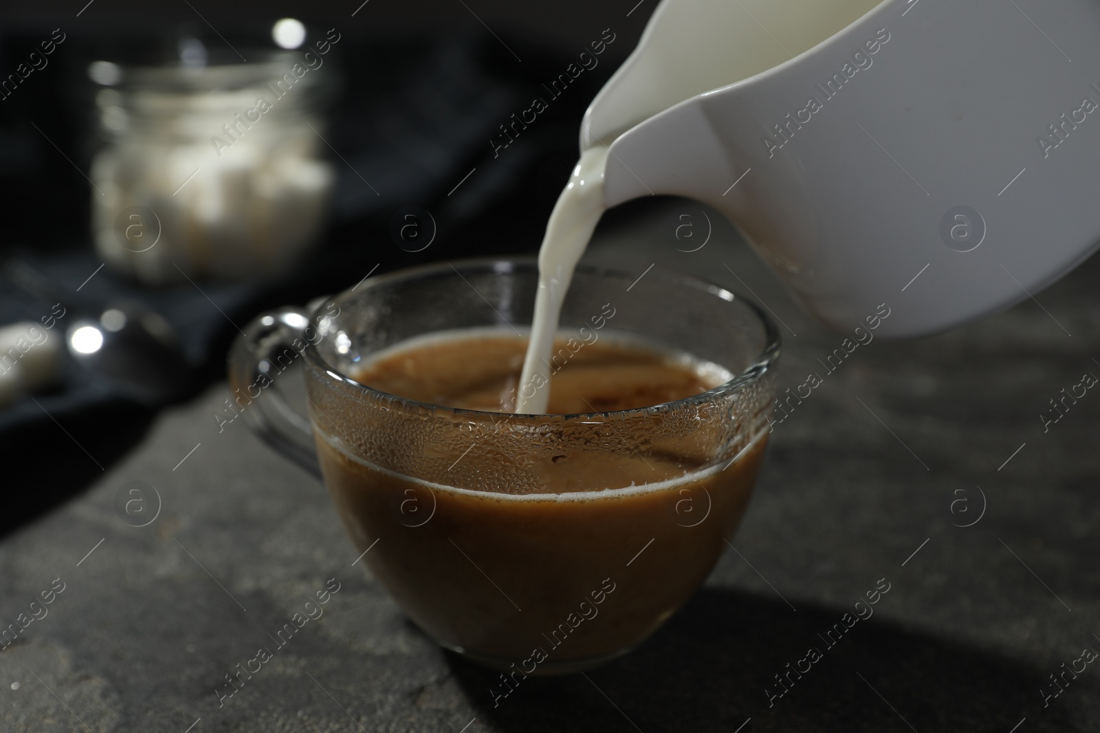 Photo of Pouring milk into cup of coffee on grey table, closeup