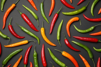 Photo of Different colorful chili peppers on black background, flat lay
